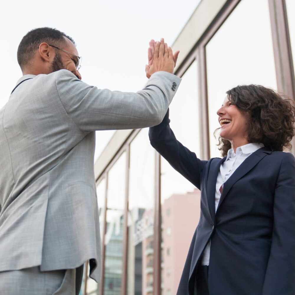 08-icf-guide-experience-coaching-good-investment A man and woman high five each other in an outdoor city landscape celebrating their investment in their growth