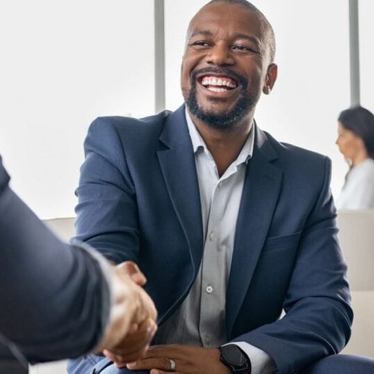 Organization Coaching A smiling professional shaking hands with another professional in a light-filled, modern lounge.