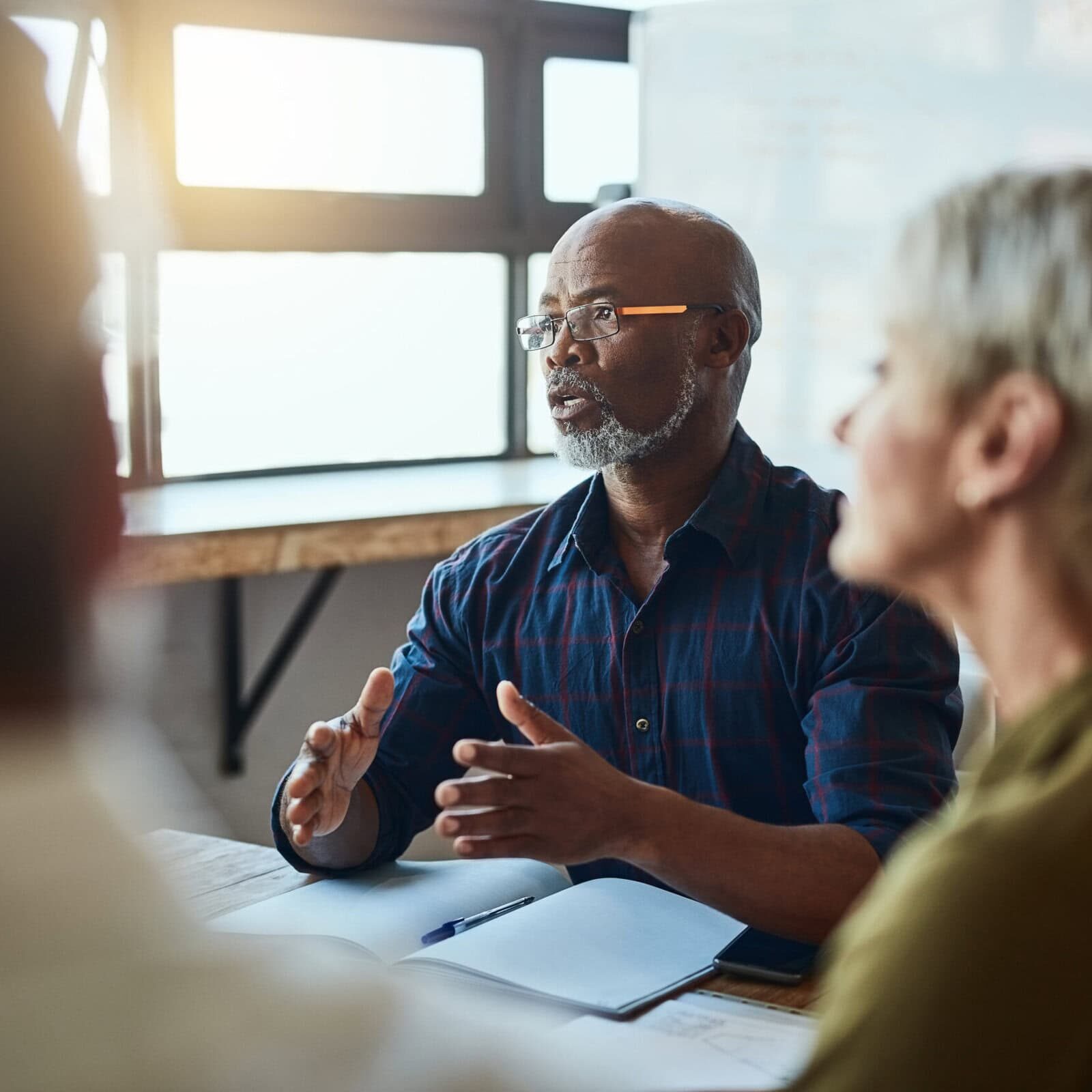 Business people, meeting and leadership of black man in office, talking or speaking. Teamwork, ceo and senior African male professional brainstorming, collaboration or planning strategy in workplace. A man holds a meeting in an office and is talking and speaking with the other professionals in the room to collaborate on a project