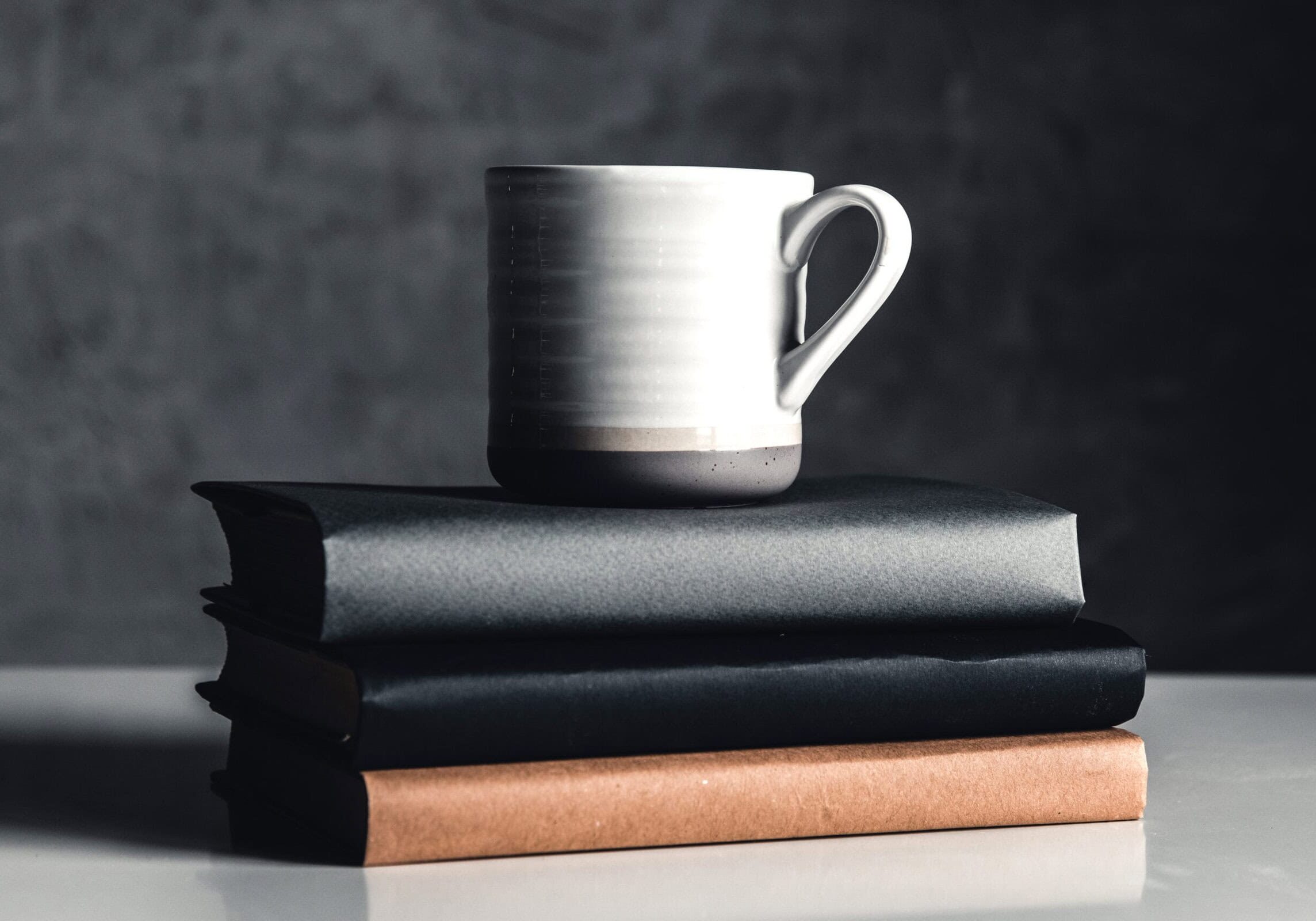 A cup of coffee on stack of books on grey background Books stacked with a ceramic coffee mug on top, symbolizing a reflective learning environment for coaching education