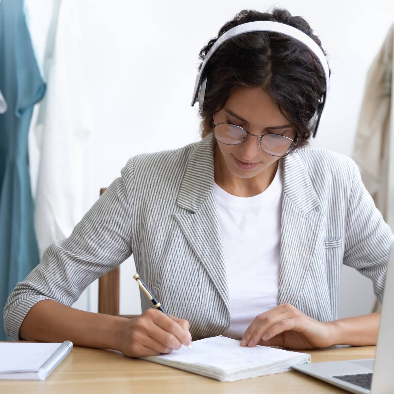 Caucasian woman in headphones study online on computer Student in a virtual coaching education session, taking notes while attending an online webinar for professional development