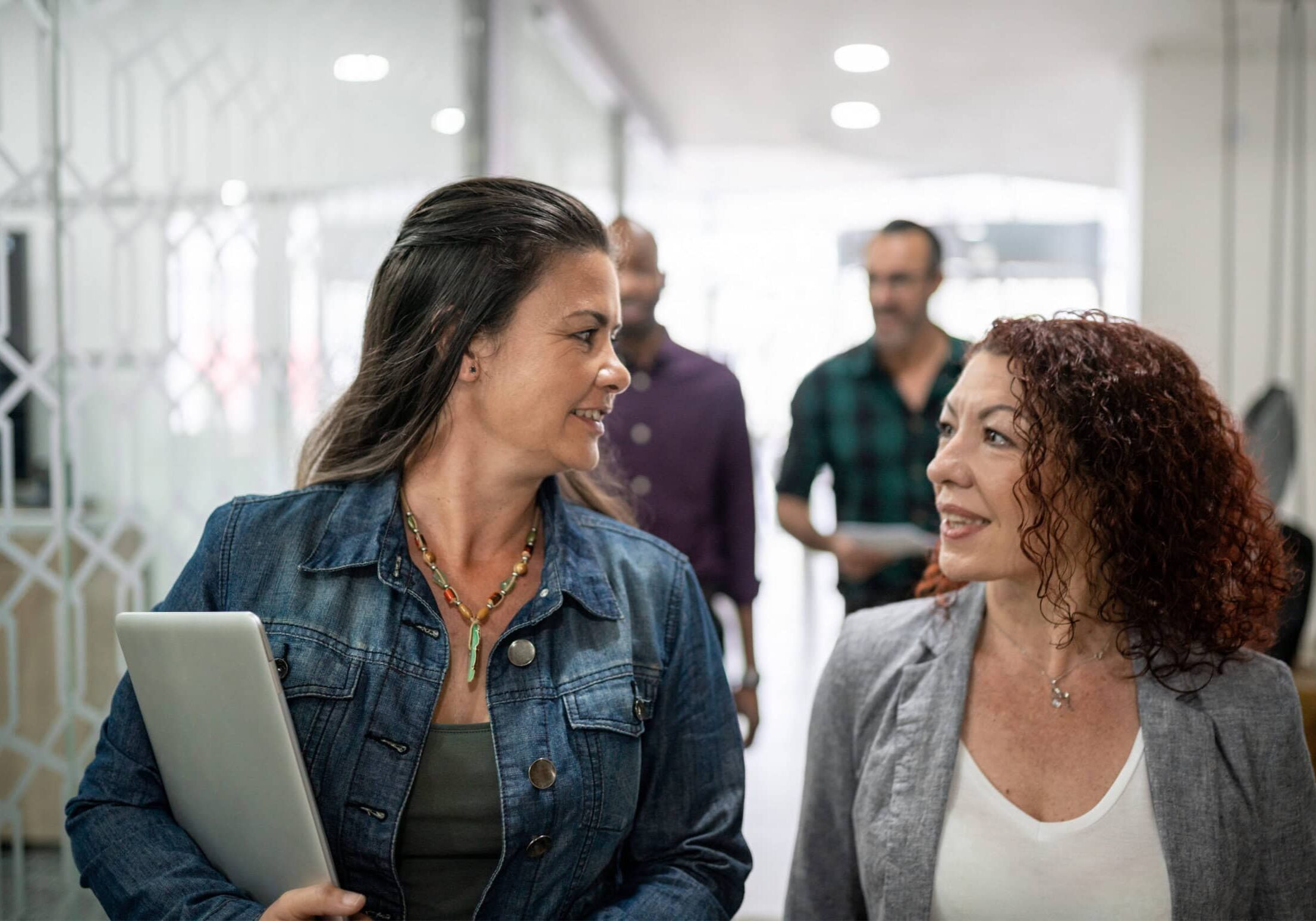 Collaborative Coach Conversation Two women walking and having a collaborative coaching conversation in a modern office, embodying a friendly work environment.