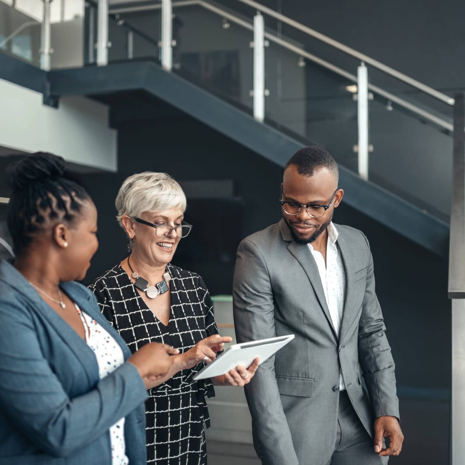 Three corporate business people walking out of a successful meeting, smiling discussing information on an digital tablet ICF Foundation leaders discussing global coaching programs