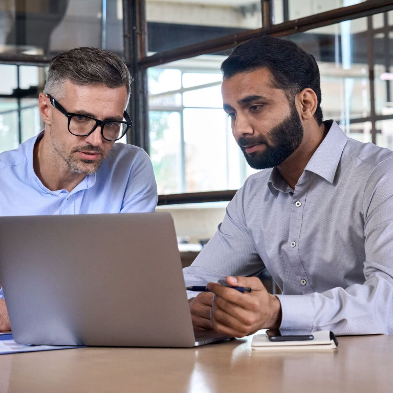 icf-credential-actc-exam-registration Two men look at a laptop to registration for an exam in a professional office