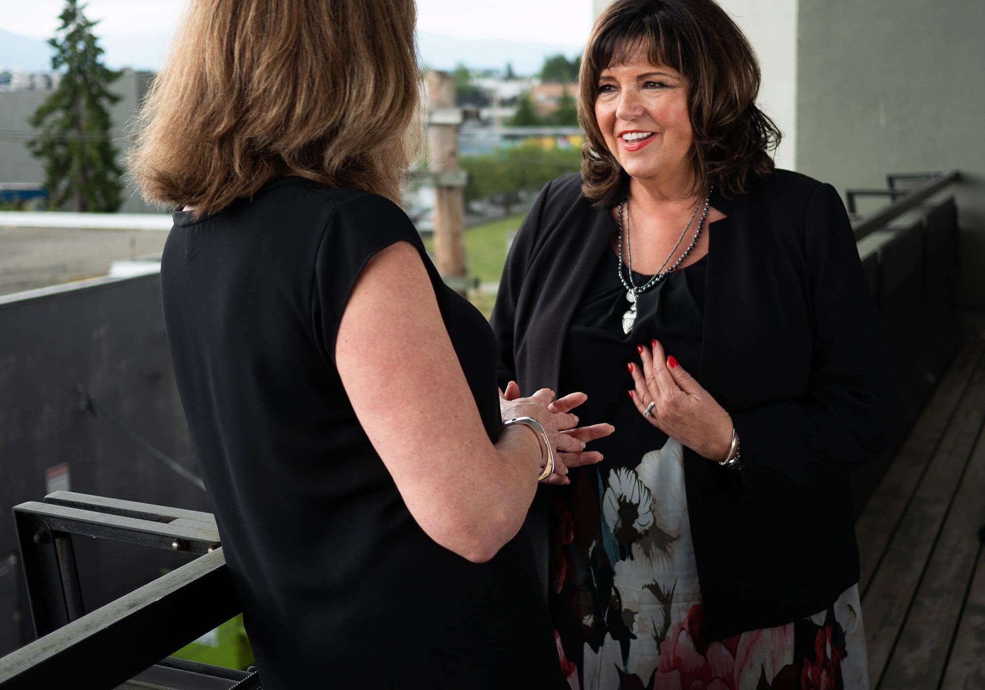 Experience Coaching: Judy's Story Two women having a professional coaching discussion on a balcony, emphasizing personal and career development.