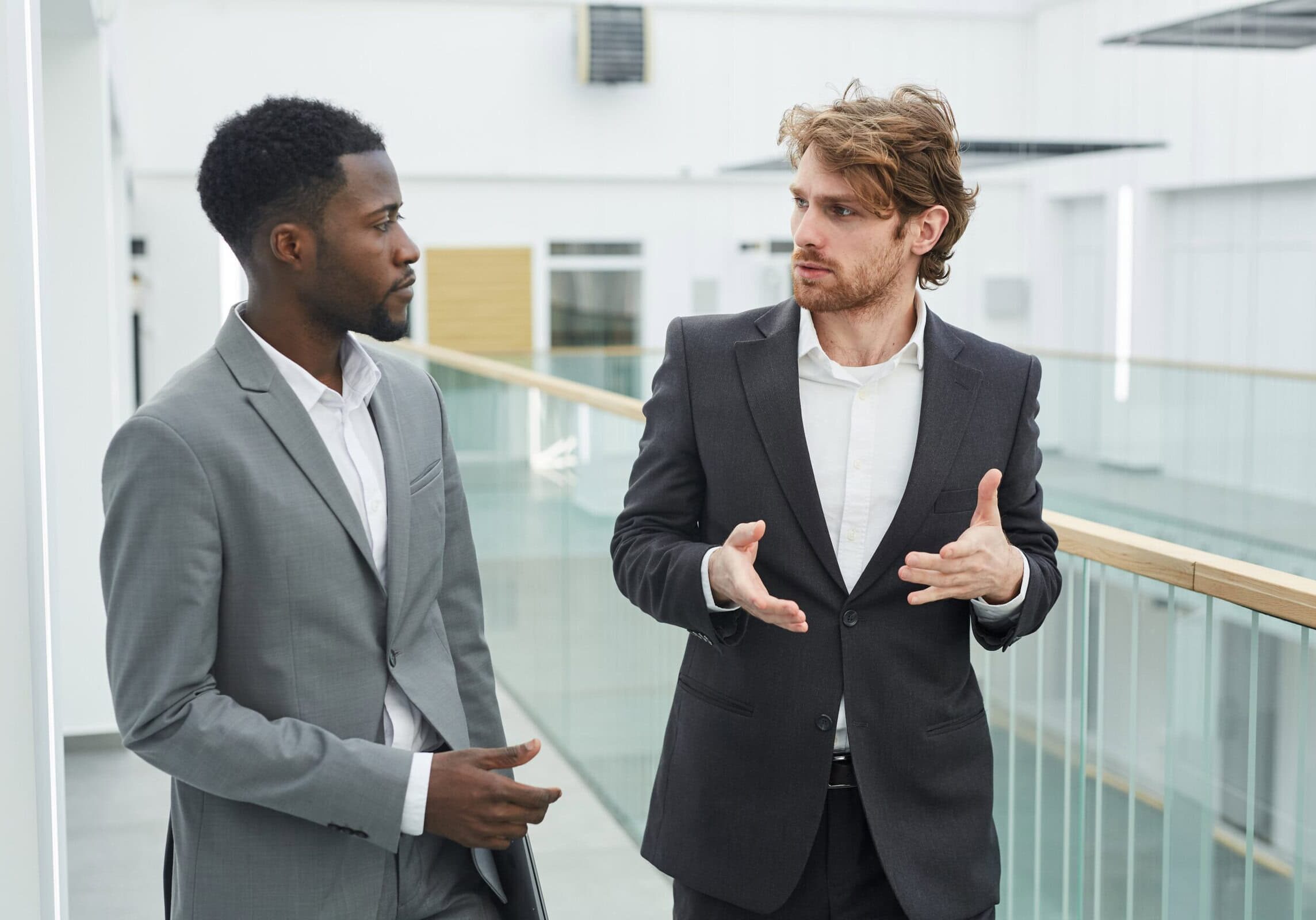 icf-professional-development-coaching Two young men in suits engaged in an animated professional development discussion in a modern office.