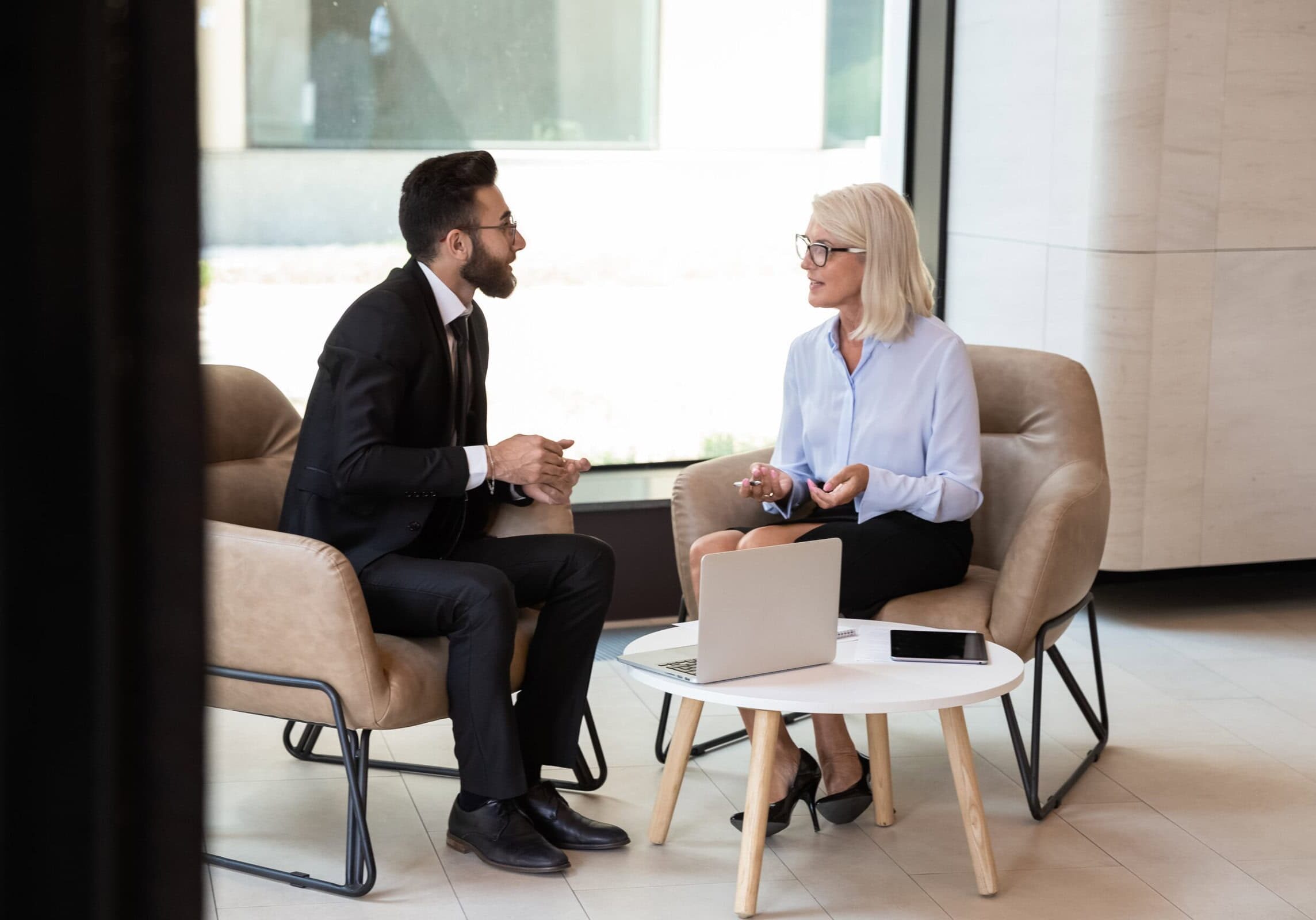 Multiracial diverse businesspeople talk discussing cooperation at meeting A variety of coaching tools, including worksheets and digital resources, displayed on a desk.