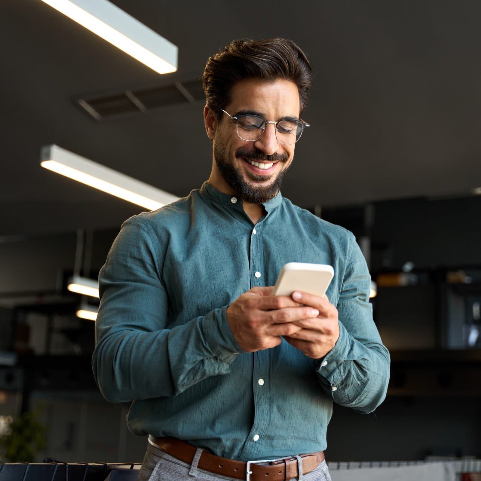 Smiling,Handsome,Latin,Business,Man,Executive,Or,Employee,Using,Cell man in button up shirt standing and smiling while looking at his cellphone in his hands