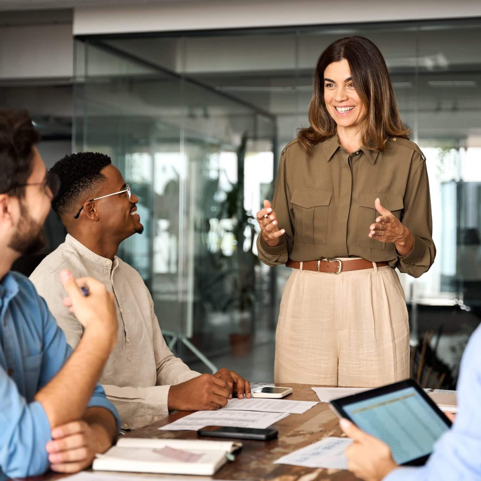 Happy,Middle,Aged,Business,Woman,Executive,Ceo,Leader,Discussing,Project smiling coach addressing three people at a conference table