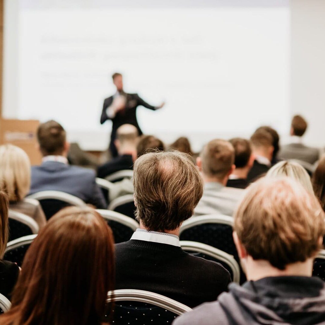 Speaker,Giving,A,Talk,In,Conference,Hall,At,Business,Event. large conference hall with speaker at the front giving a presentation
