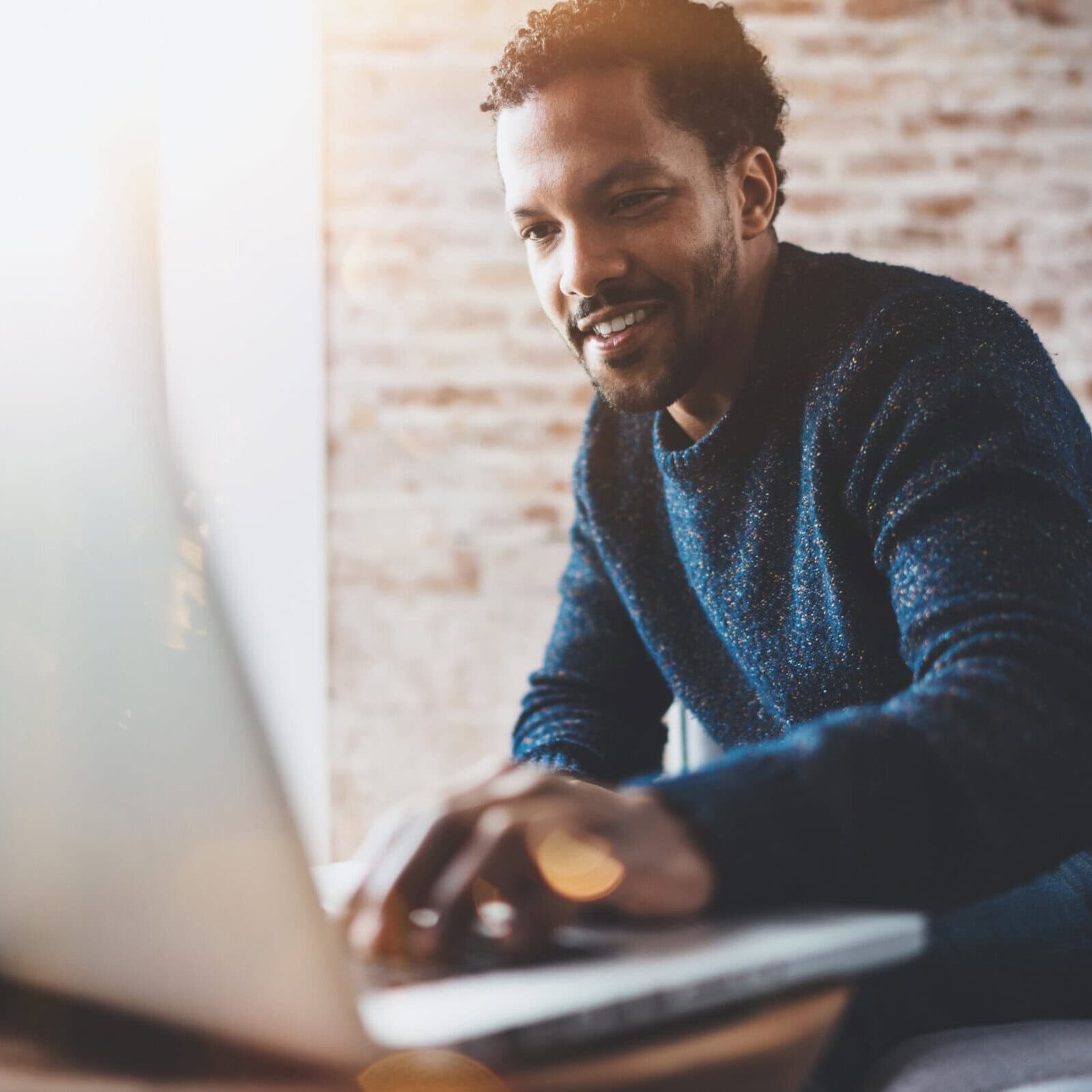 Cheerful,African,Man,Using,Computer,And,Smiling,While,Sitting,On man leaning forward to put his hand on a laptop keyboard